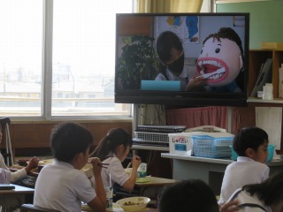 歯ブラシで歯の磨き方を教えてもらうTV放送を見る子ども