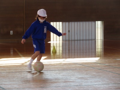 体育館でサッカーのドリブル競争をする２年２組の子ども