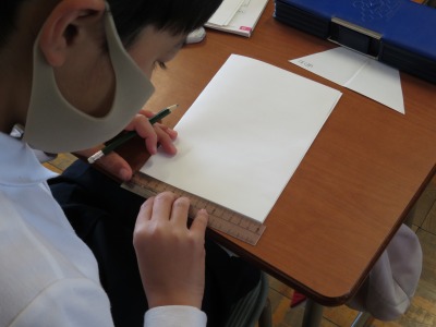 半分に折った紙を使って一辺が１６cmの正三角形を作ろうとしている３年２組の子ども